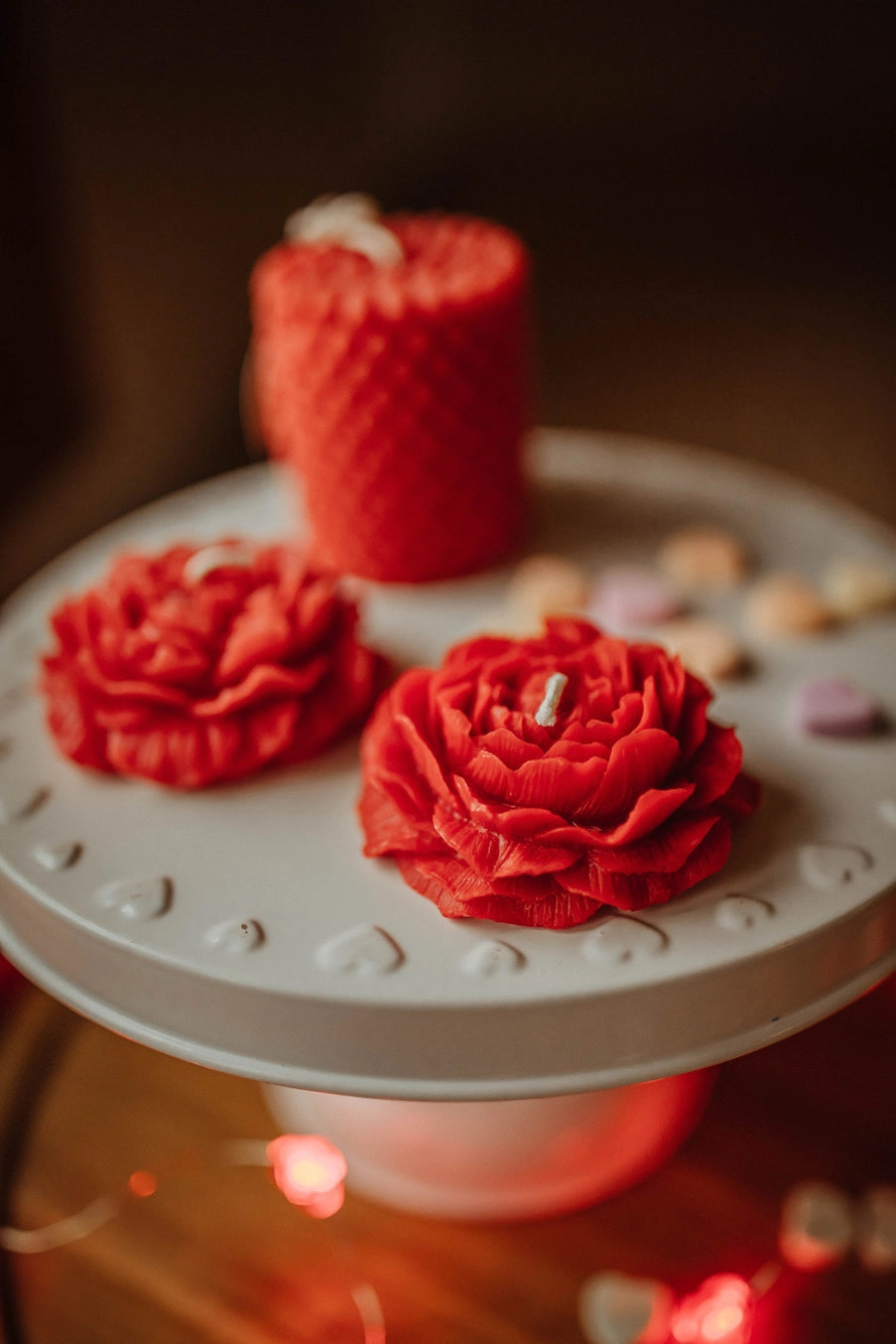 Red floral decorations on a white cake stand with a blurred red candle in the background. ©The Holten Homestead
