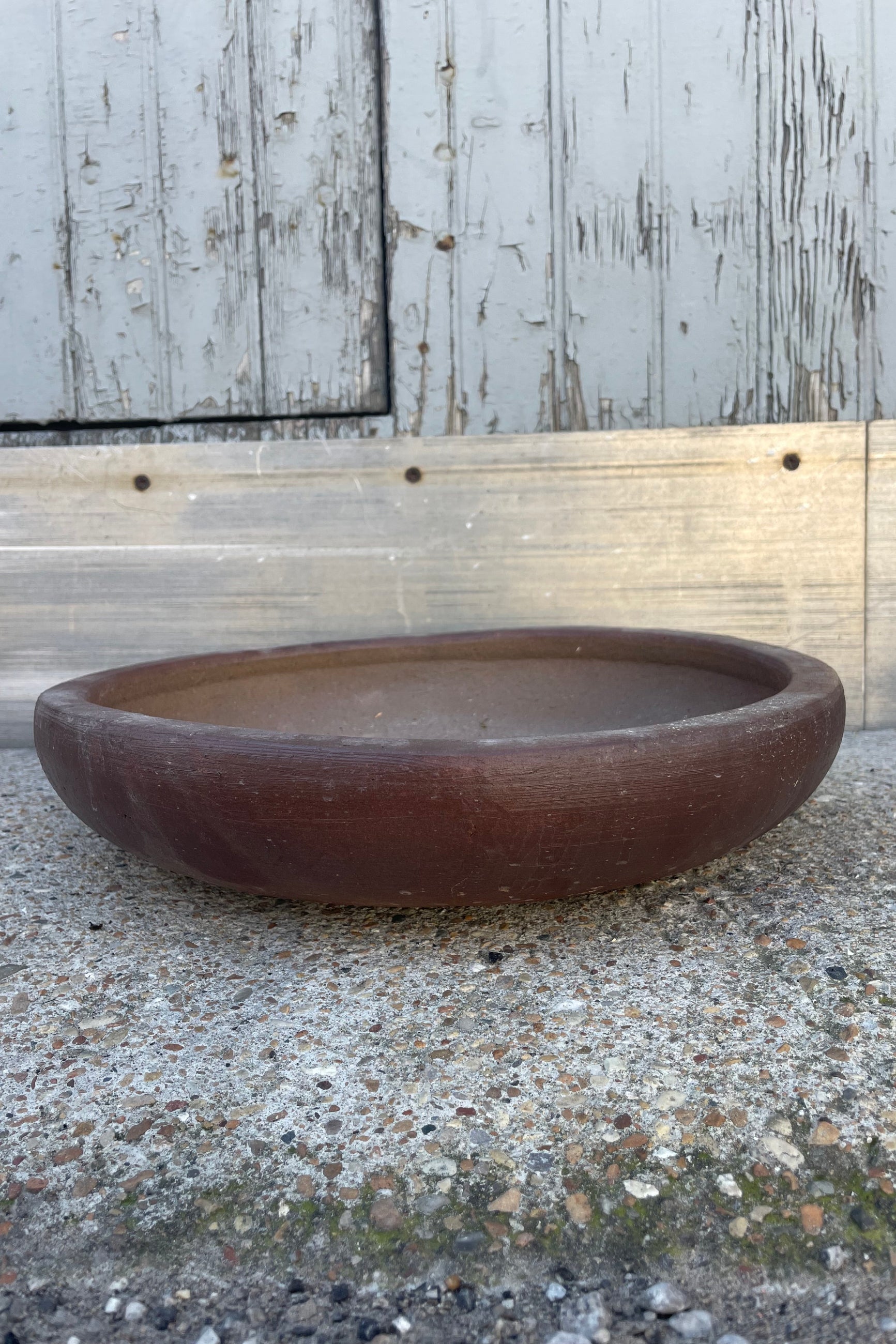 Photo of a low ceramic bowl with brown glaze in front of a textured wall ©Sprout Home