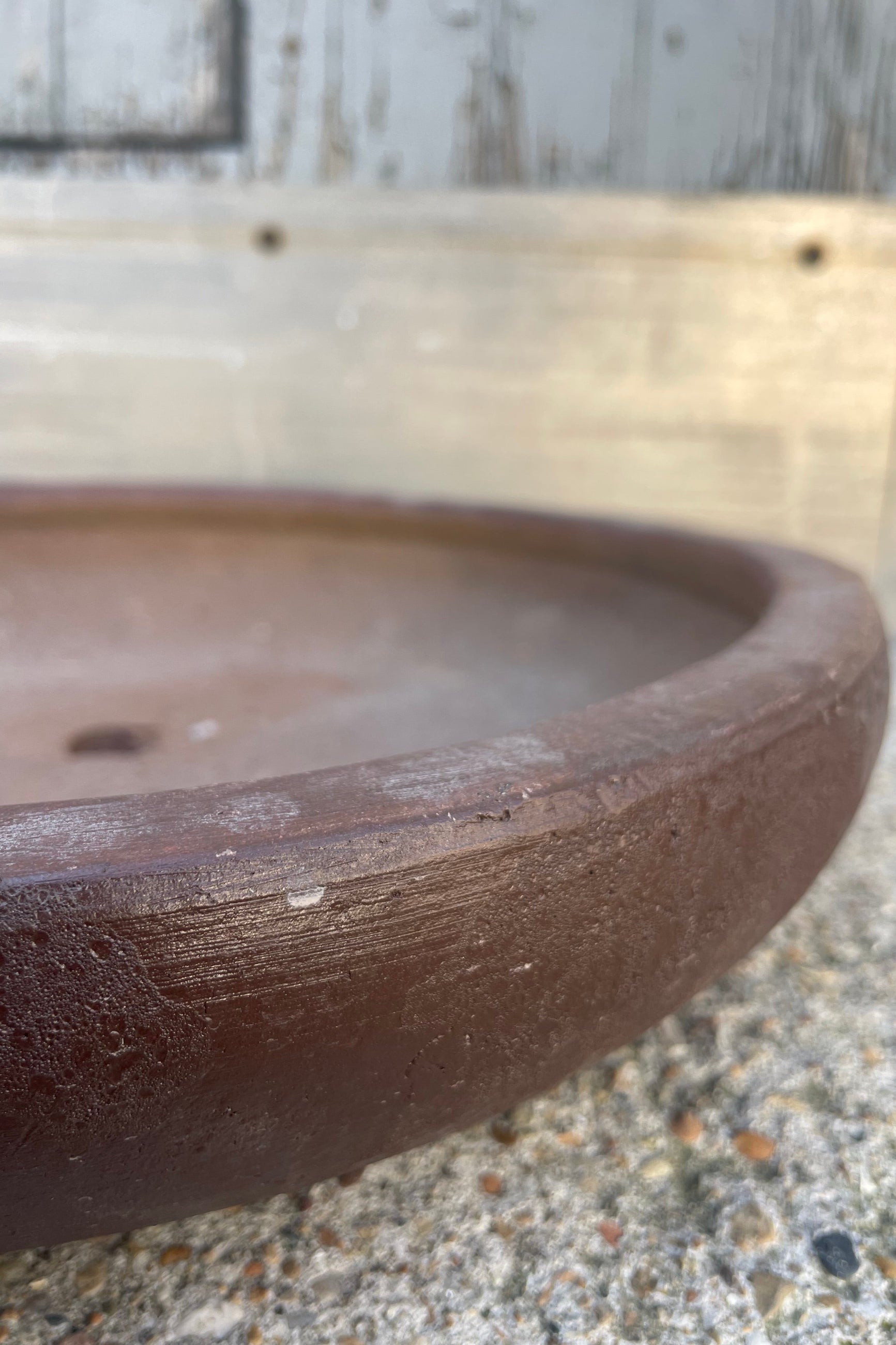 Close-up photo of a low ceramic bowl with brown glaze in front of a textured wall ©Sprout Home