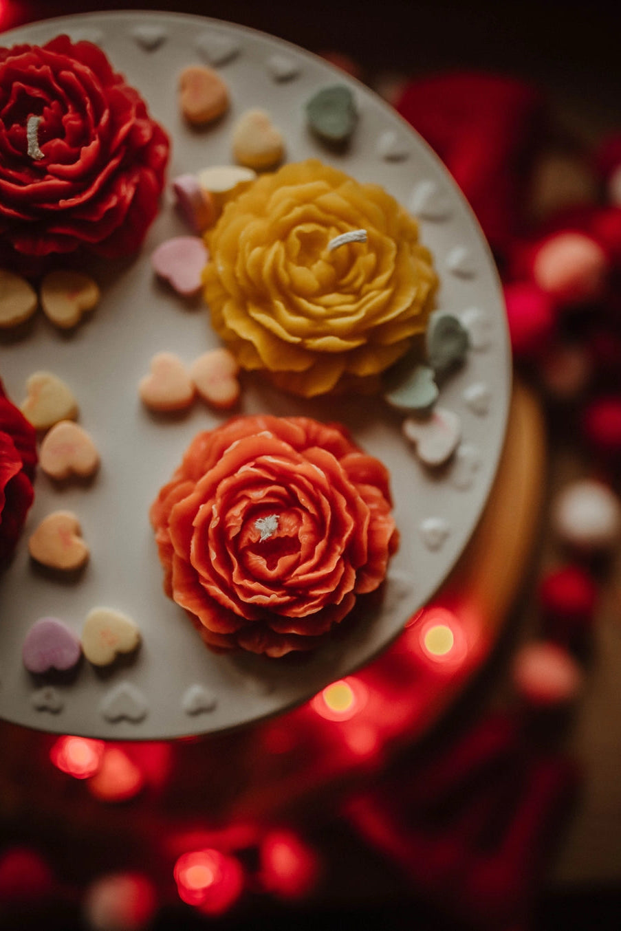 Decorative cake with red, yellow, and orange flowers on a white base, surrounded by blurred lights. ©The Holten Homestead