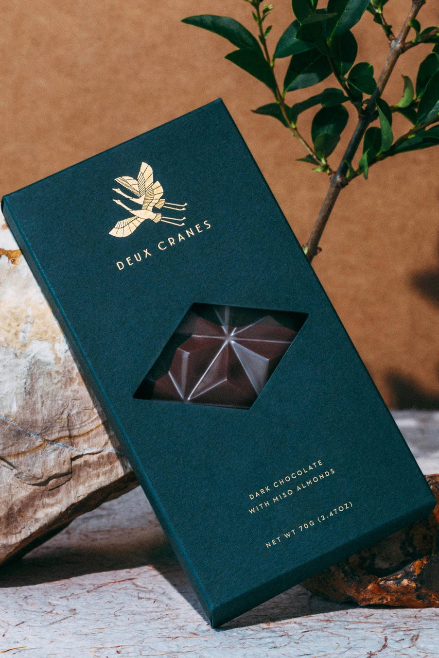 Dark chocolate bar in a green packaging with 'Deux Coanes' branding, placed on a natural stone surface.  ©Deux Cranes
