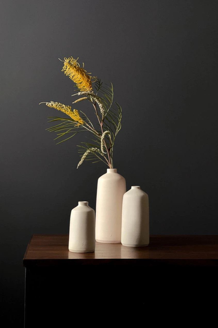 A series of three different sized Ivory Bud vases by L'Impatience Pottery on a wood credenza.