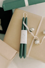 Mo & Co beeswax taper candles in Forest Green sitting on a wrapped present.