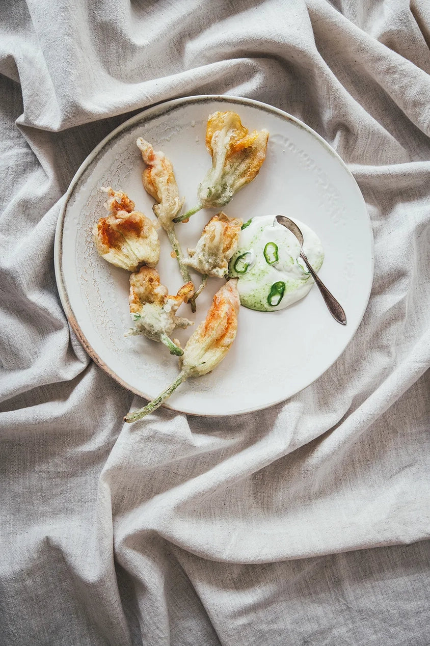 A page from the Flowers on a Plate Book showing zucchini blossoms  on a white plate sitting on light gray fabric.