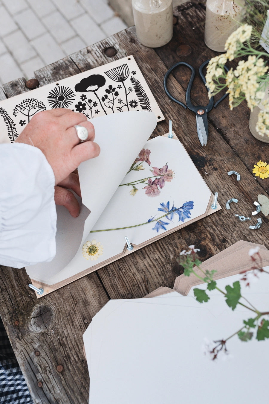 Person working with floral designs pressing them in a Studio Wald press on a wooden table ©Studio Wald