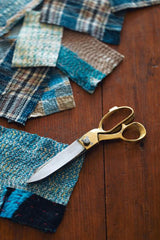 Brass & Steel scissors by Fog Linen Work next to some fabric samples on a wooden table. 