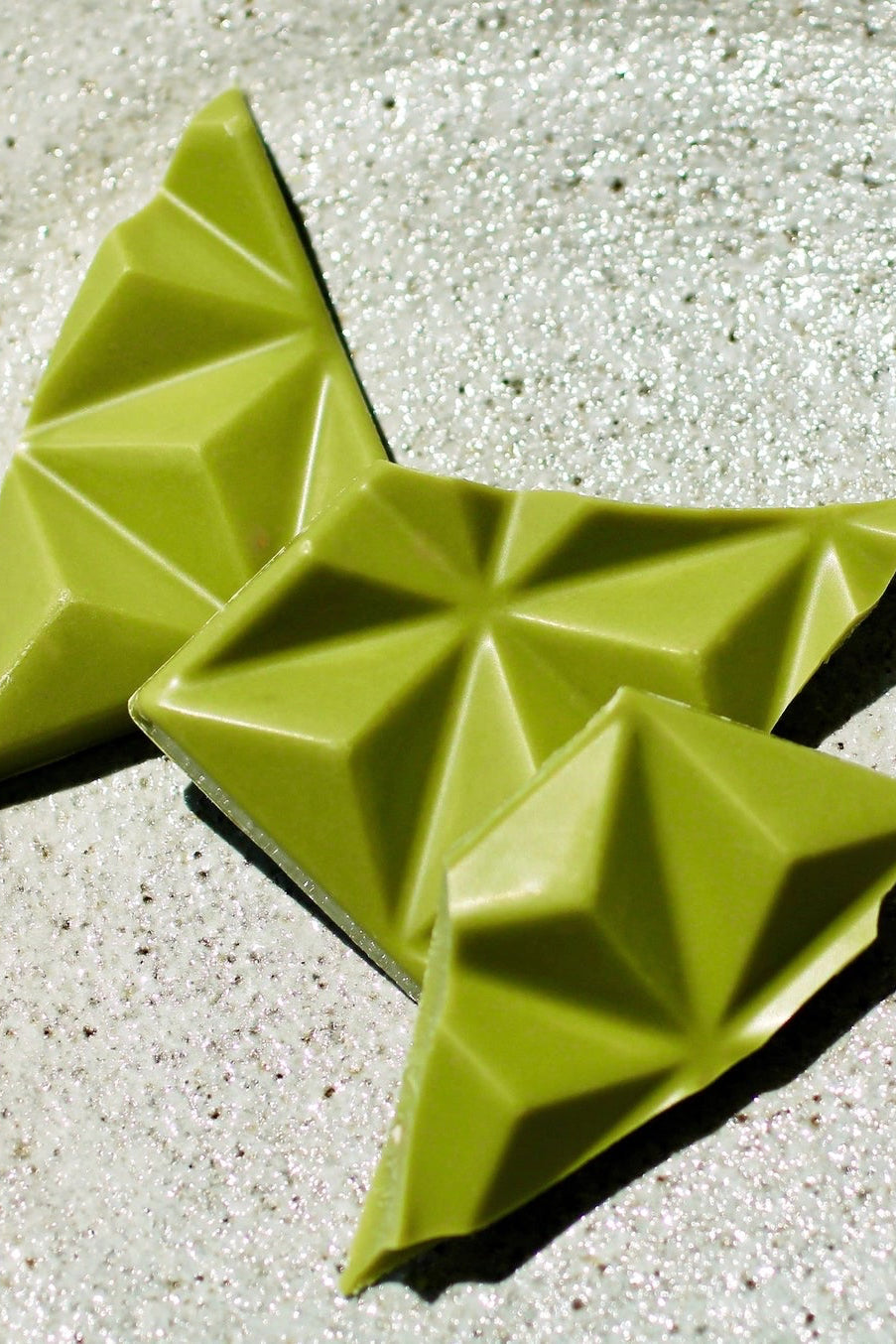 Green geometric butterfly-shaped pieces of Matcha Chocolate bar on a textured surface ©Deux Cranes