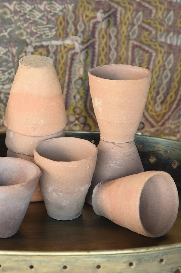 Terra cotta cup by Homart shown in multiples on a table and a printed backdrop.