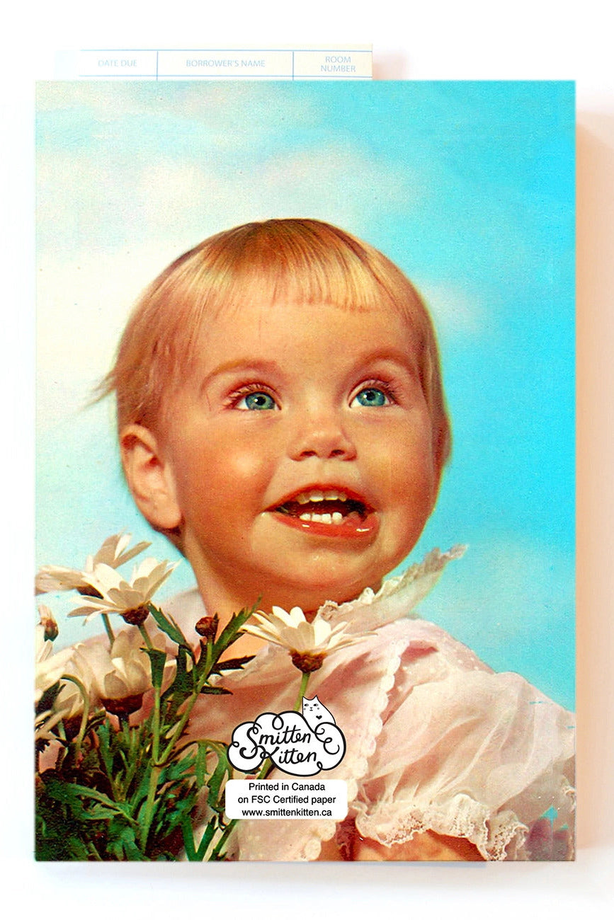 A vintage-style Carpe Diem Notebook featuring a young child with blond hair, blue eyes, and a white dress holding white flowers against a bright blue sky background. The card has a visible 'Smile Miller' logo near the bottom and is photographed against a plain white background. ©Smitten Kitten