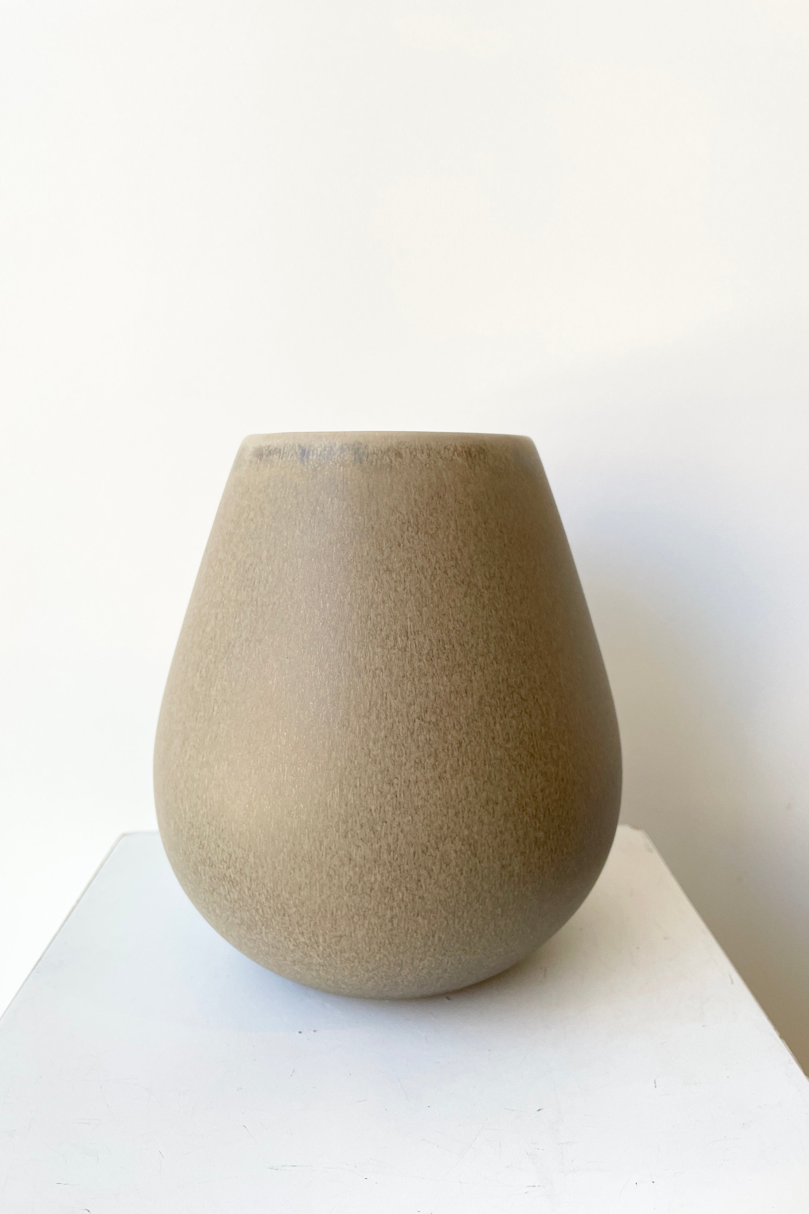 The Ease round vase in Stone color against a white wall viewed at eye level.