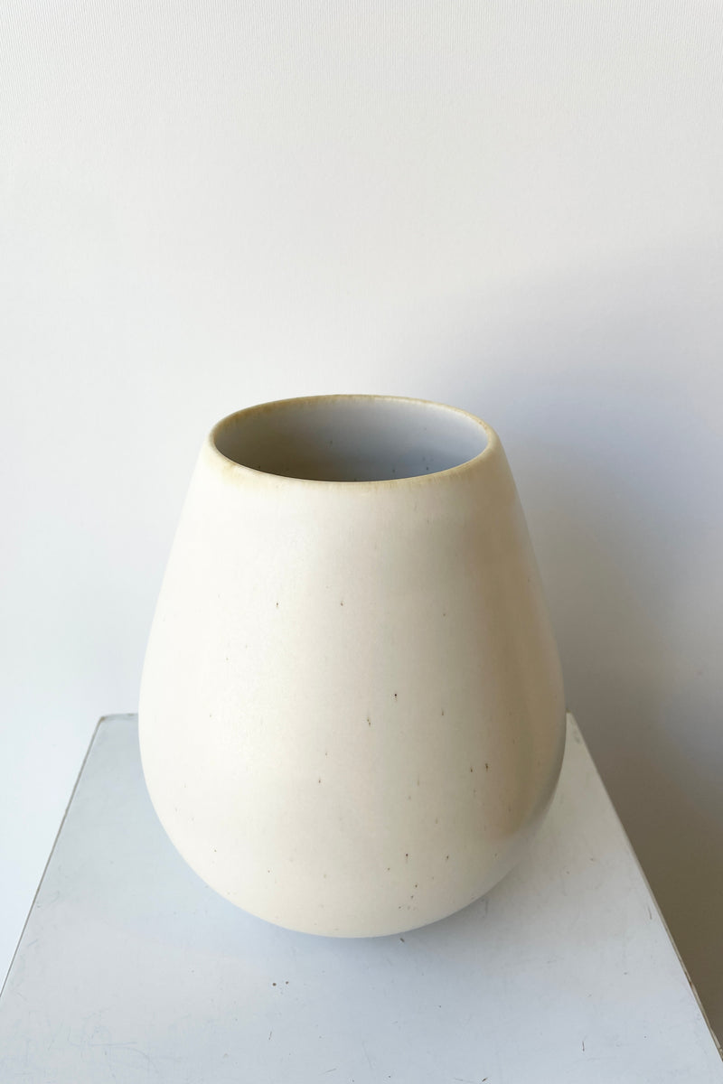 The soft shell colored Ease round vase looking from topside in against a white wall. 