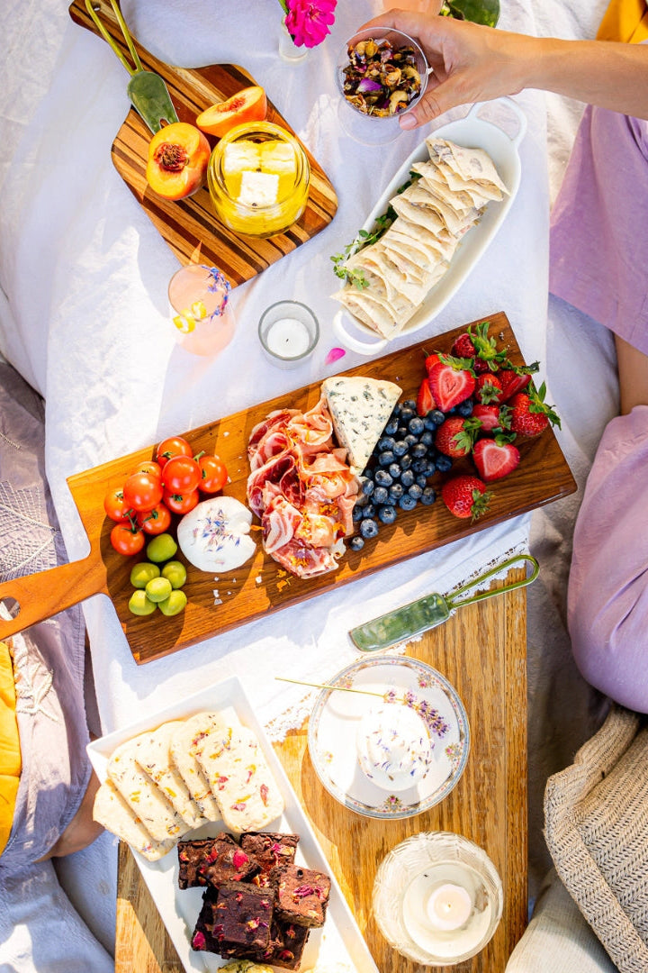 People enjoying a picnic with a charcuterie board and drinks on a blanket.  ©Flouwer Co