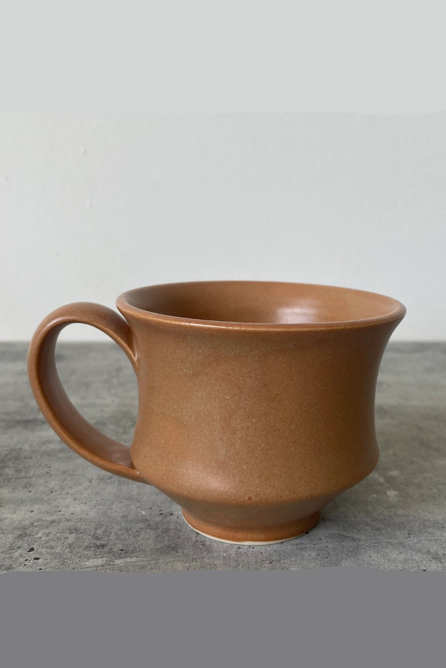 Brown ceramic hourglass mug on a gray surface with a neutral background ©Little Fire Ceramics