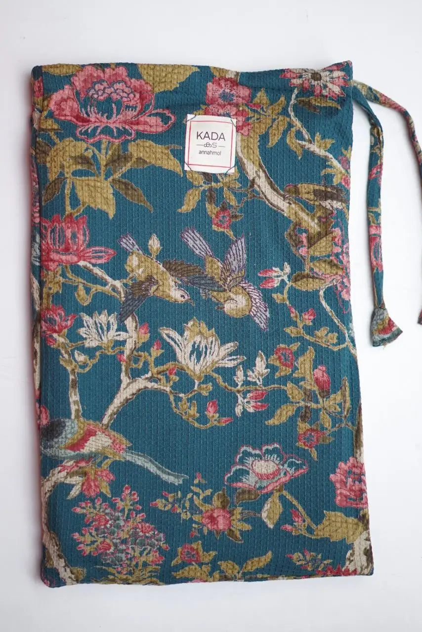 Floral drawstring bag with a visible brand label of the Waffle Cotton Beach Towel w/ Pouch Blue Fleur on a white background ©Annahmol