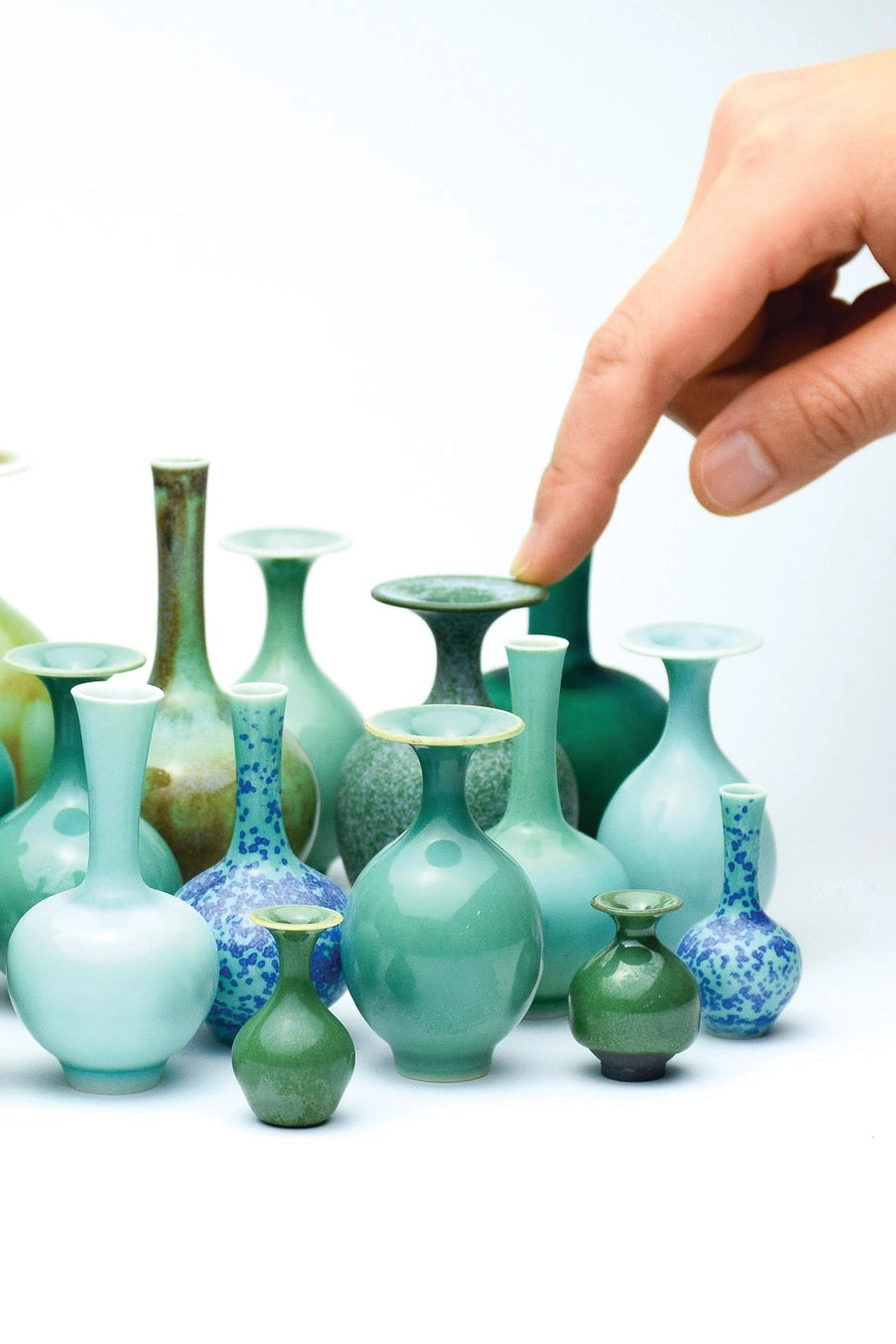 Collection of green ceramic vases with a hand reaching out to touch one. ©SGW Labs