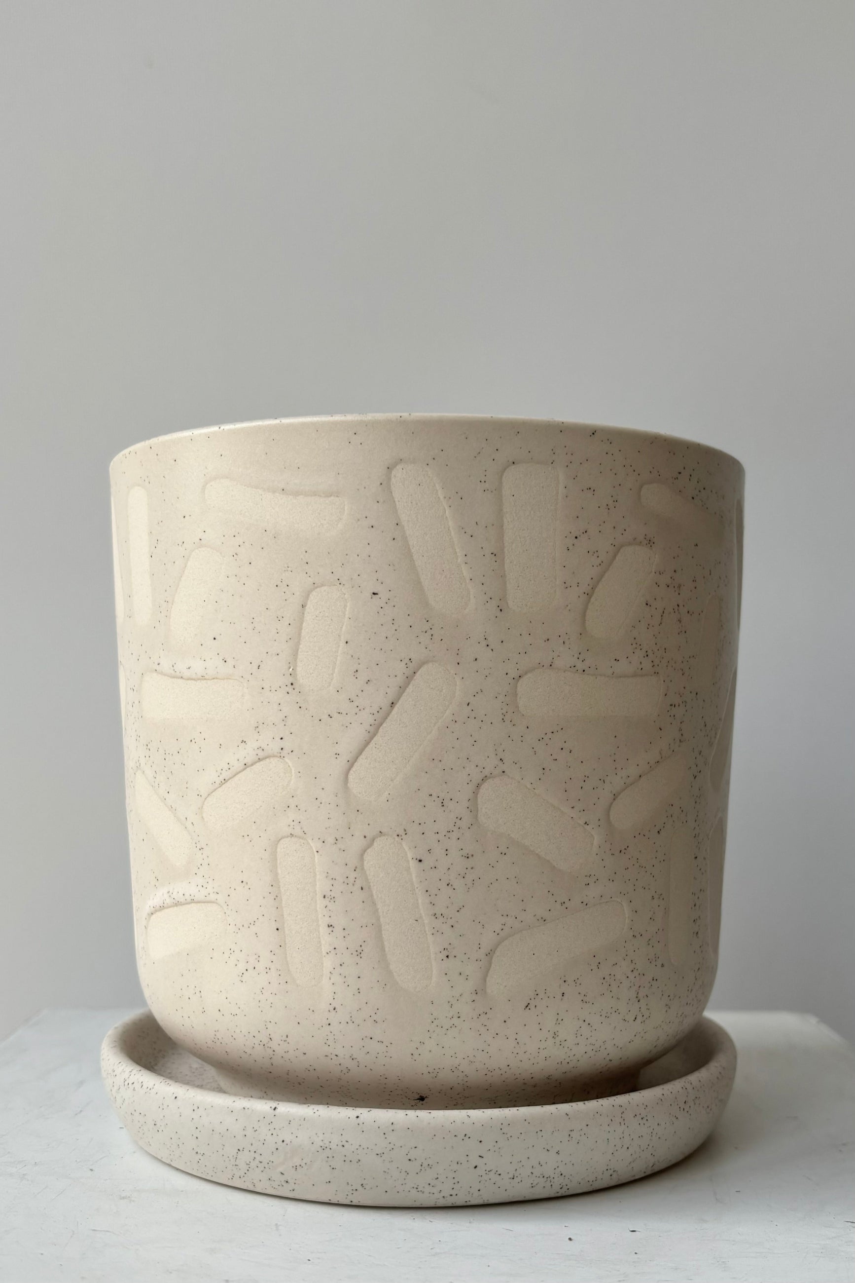 The Sundae Pot features a sesame glaze with stamped shapes scattered across the surface against grey wall ©Sprout Home