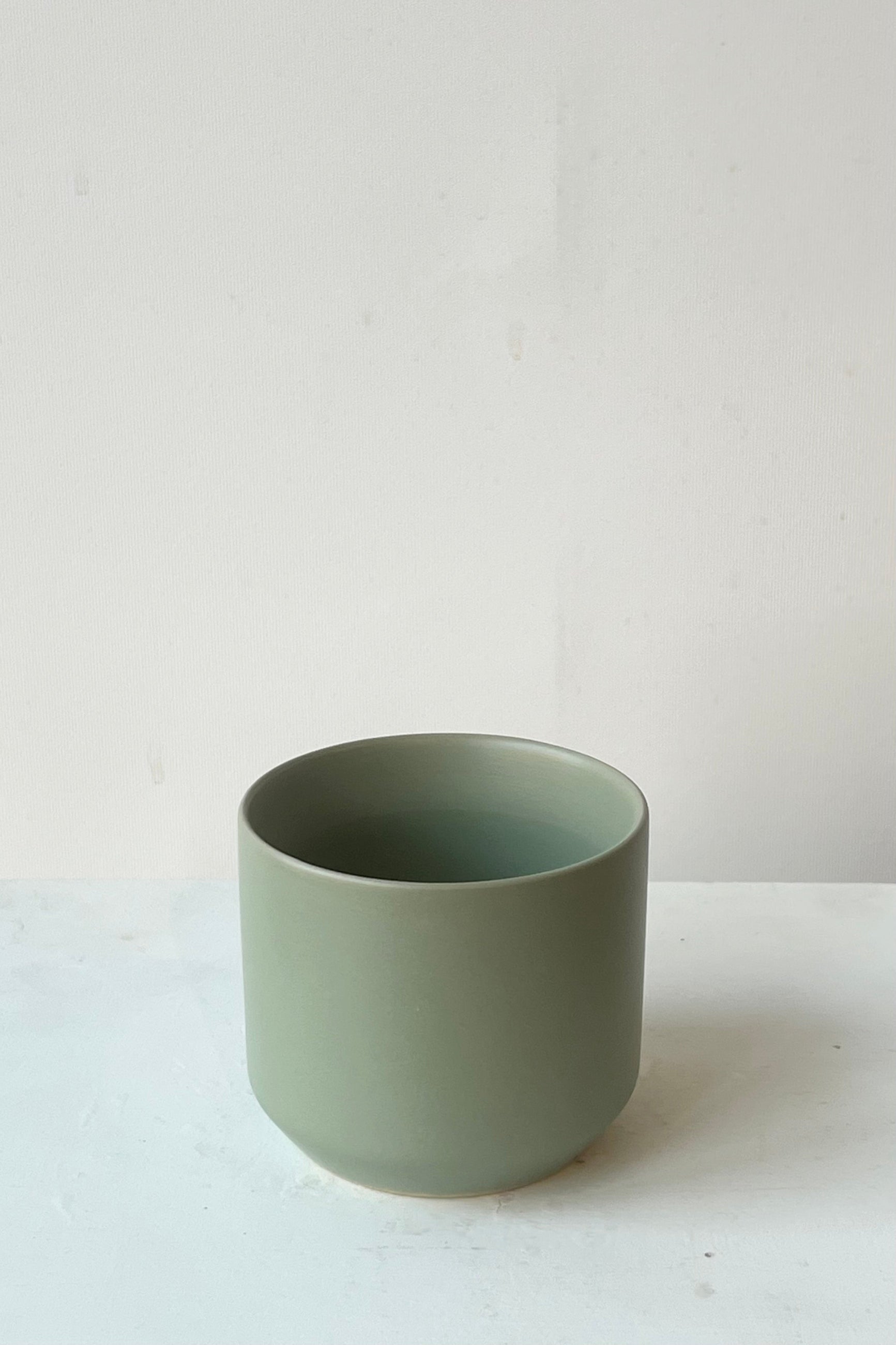 Green ceramic cup on a white surface with a light gray background ©Sprout Home