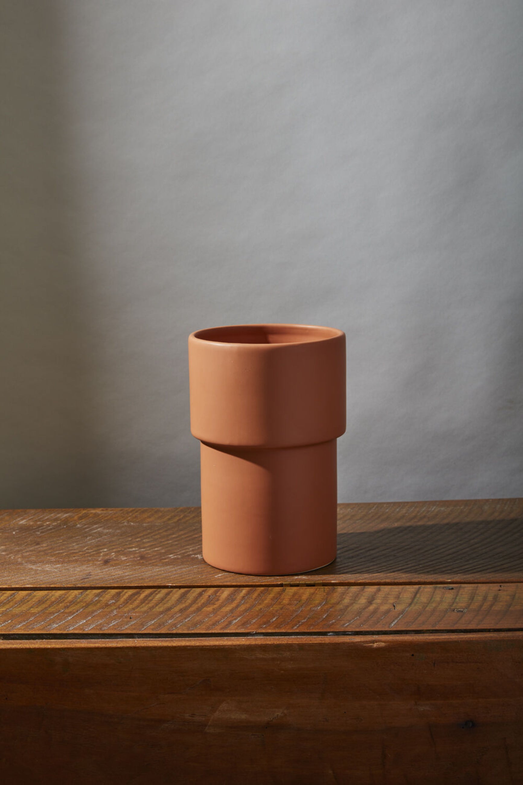 A footed Vermillion vase on a wood surface and gray background. 