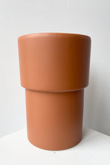 The Vermillion vase viewed from the side against a white wall showing the two tiers of its form. 