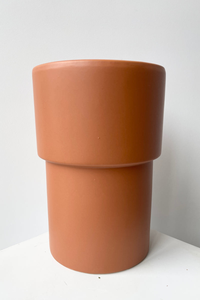 The Vermillion vase viewed from the side against a white wall showing the two tiers of its form. 