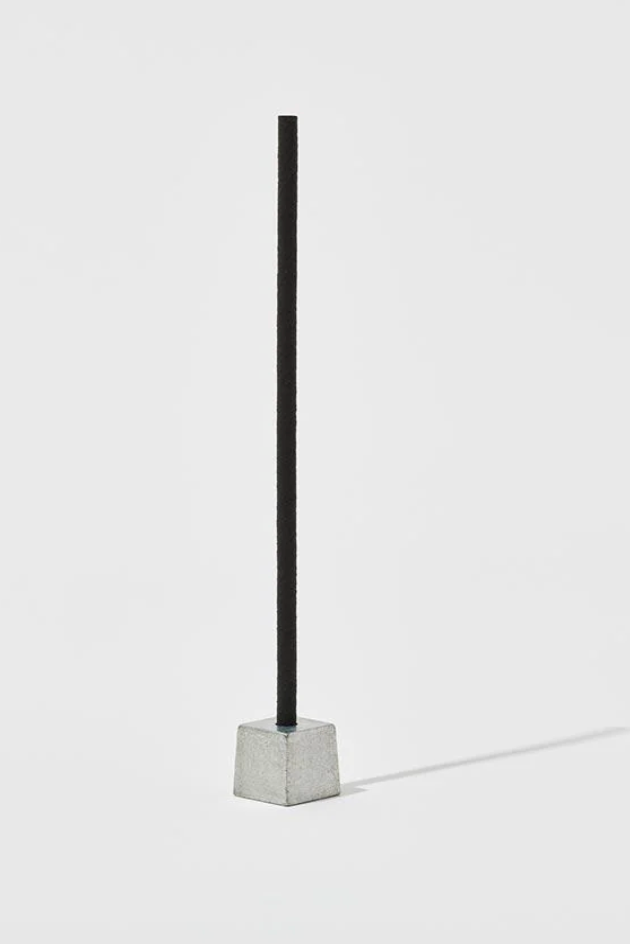 A black stick of incense in a metal weight in a white room ©Nippon Kodo