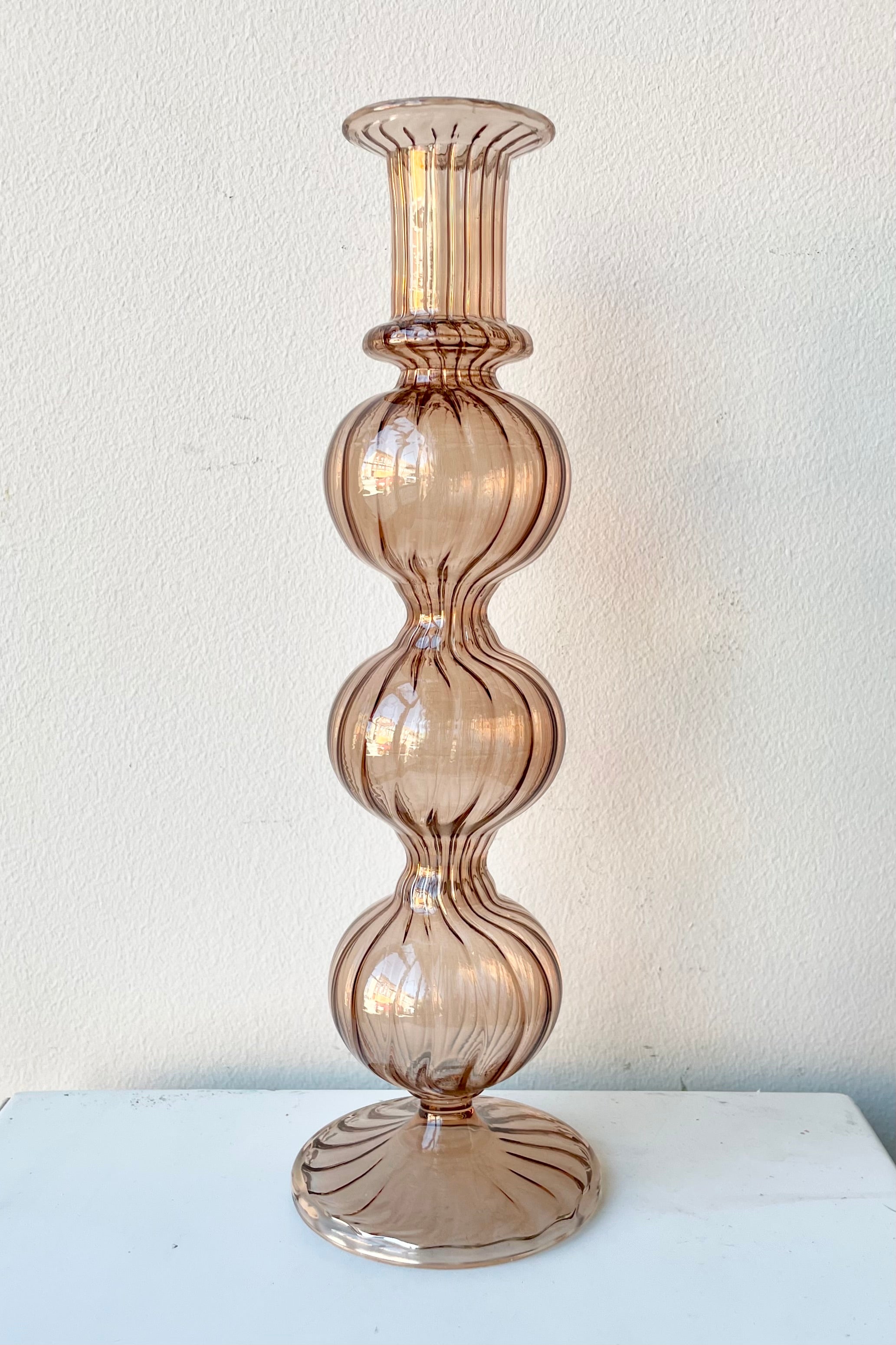 Amaranth Nalia glass candlestick holder against a white wall. 