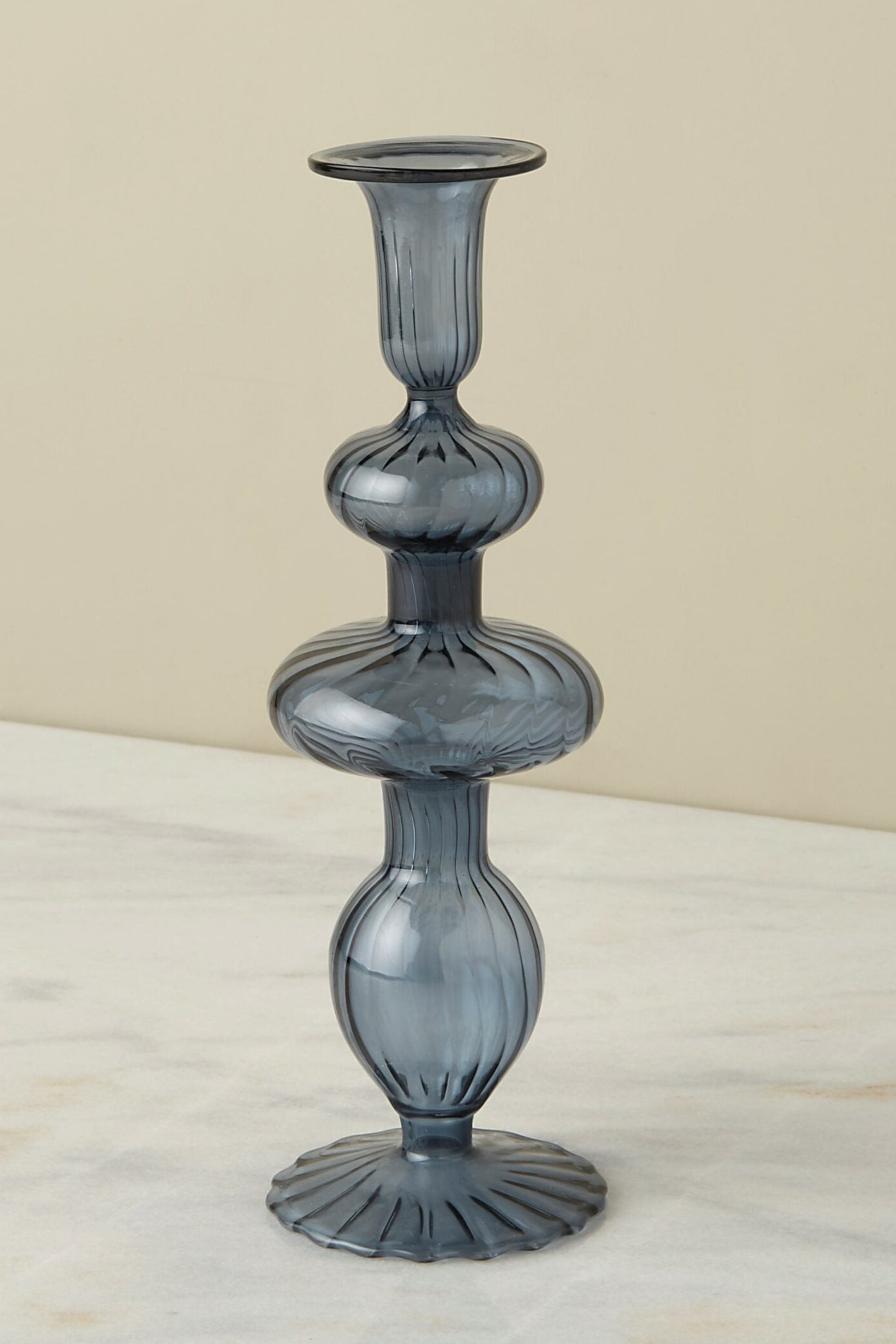 A dark blue glass candlestick holder in front of a white wall ©Sprout Home