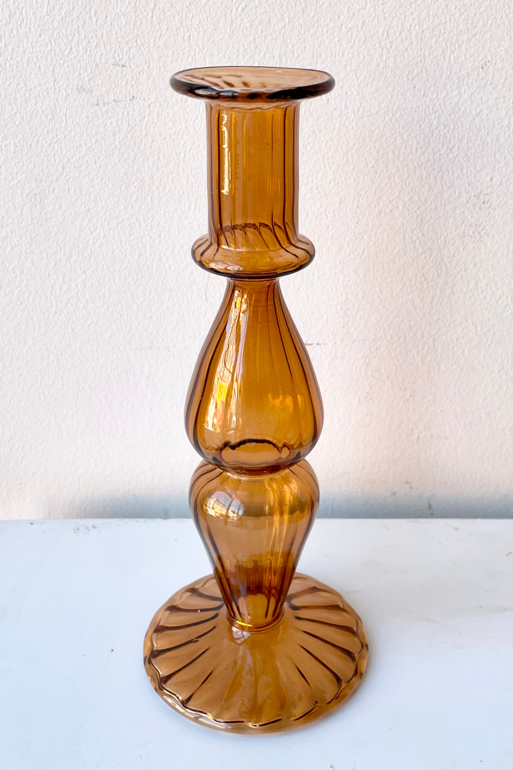 Nalia Glass candlestick holder in Marmalade against a white wall.