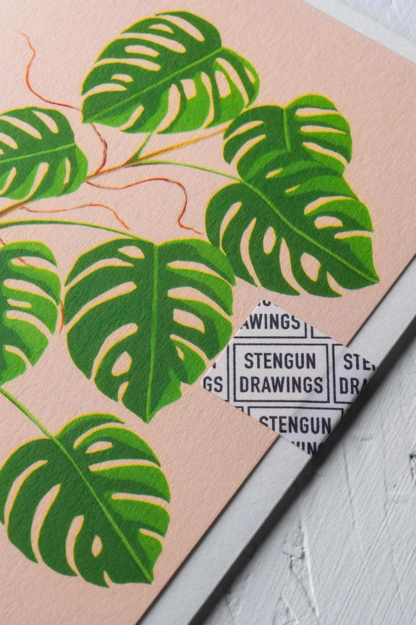 Monstera greeting card by Stengun Drawings detail of the upper right corner showing the green leaves on pink background.