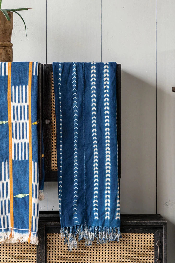 Indigo Tie dye mud cloth hanging on a shelf in front of a white painted wood plank wall