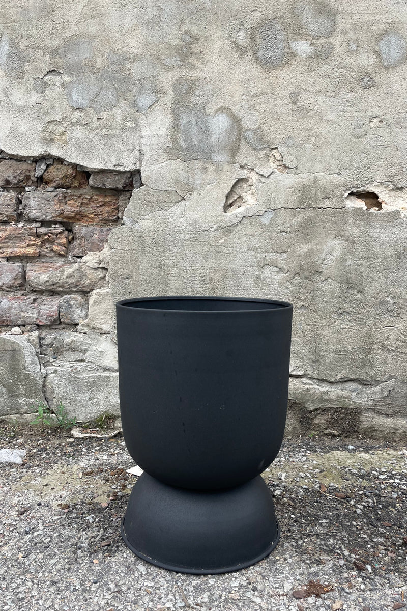 Photo of a Black Metal Compote Pot against a cement wall.