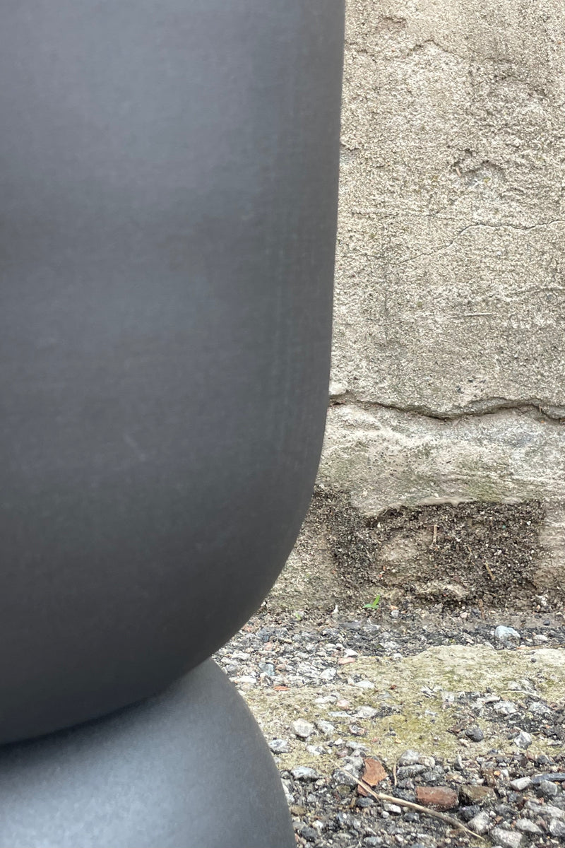 Photo of the side of a Black Metal Compote Pot against a cement wall.