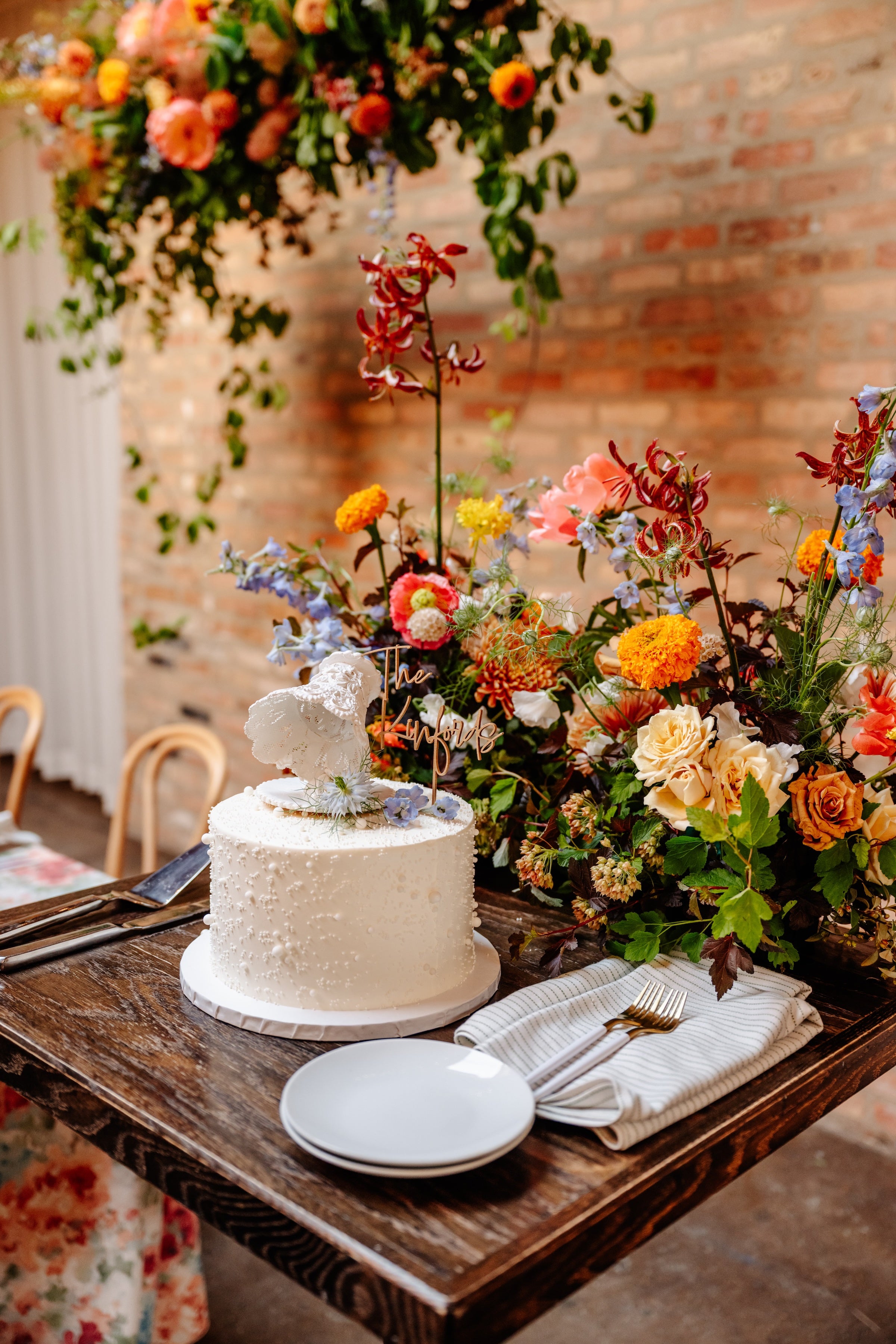 Wedding cake with floral decorations on a wooden table against a brick wall at The Arbory in Chicago. Floral by Sprout Home ©Joy by Jo Photography