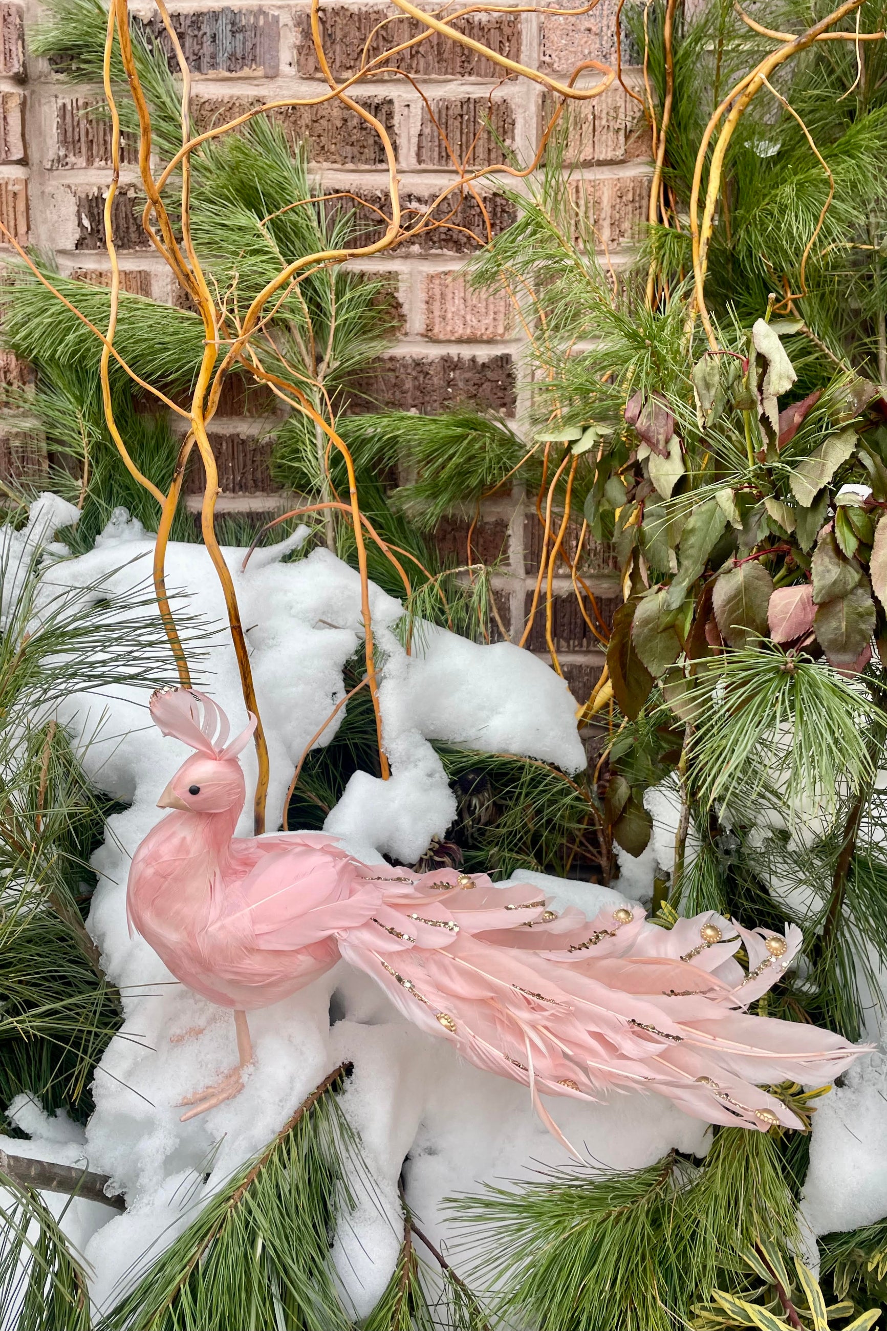 A decorative pink peacock atop snowy evergreens ©Sprout Home