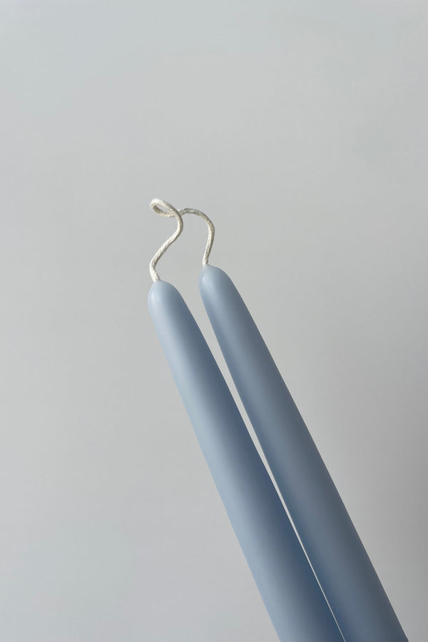 Photo of the top portion of a pair of bee's wax taper candles. The candles have a connected white wick joining them. Candles are photographed in a white room against a white wall.