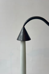 Close photo of a black metal candle snuffer placed over the tip of a pale blue taper candle. The object pair is shown against a white wall.