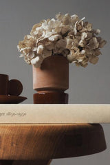 Rosa & Rusty Red Hoff Pot by Bergs Potter with a hydrangea bloom inside sitting on a side table and book. 