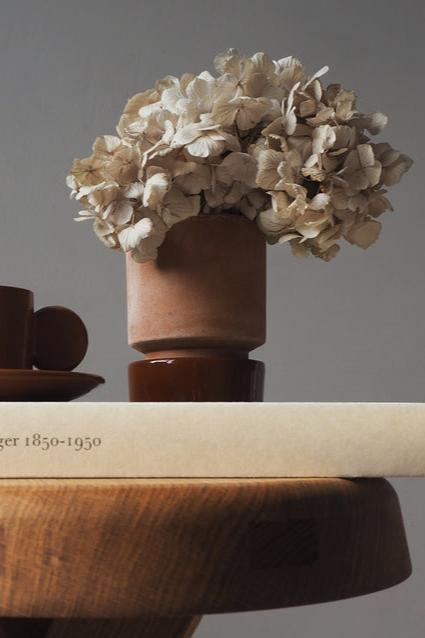 Rosa & Rusty Red Hoff Pot by Bergs Potter with a hydrangea bloom inside sitting on a side table and book. 