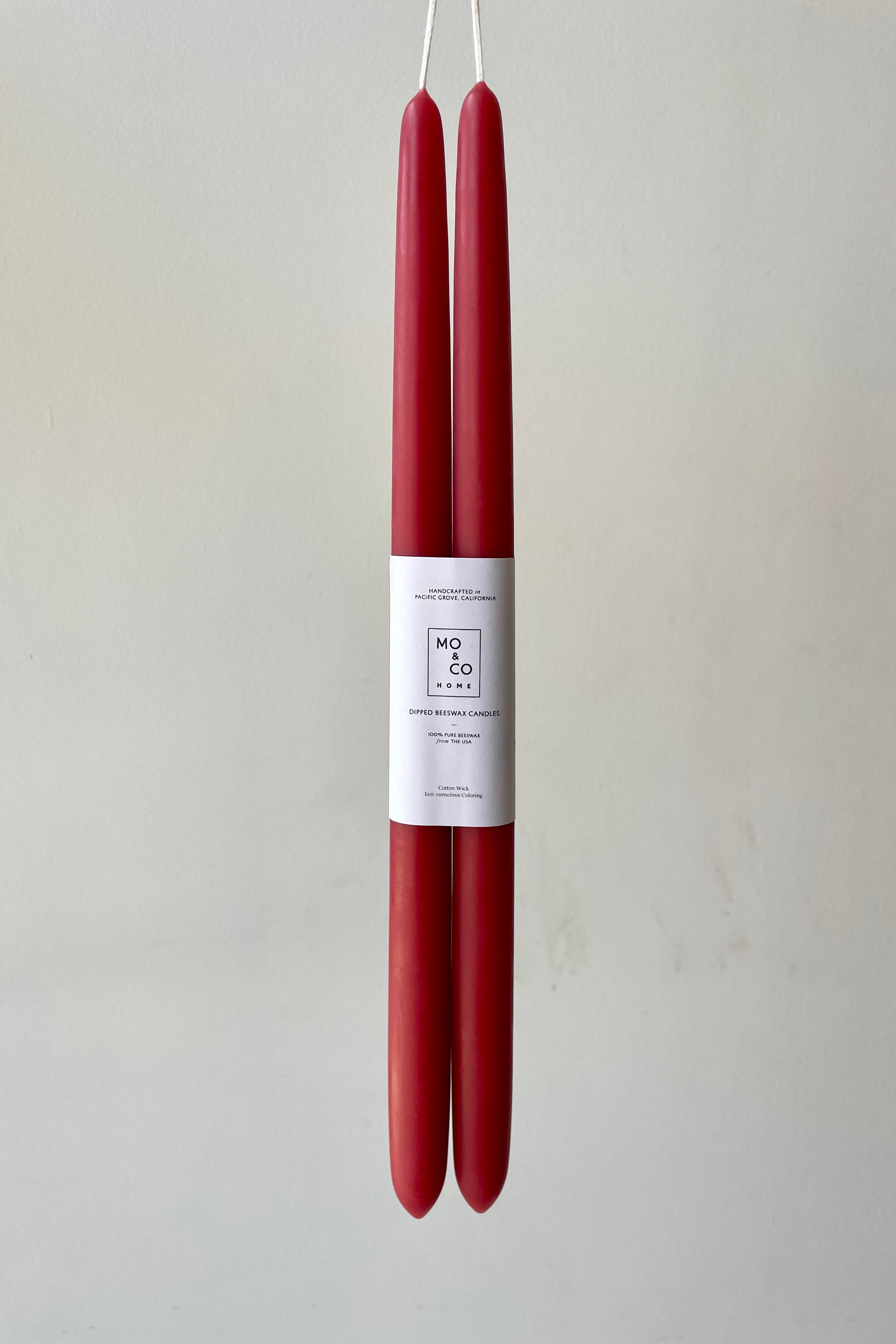 A pair of berry red beeswax taper candles against a white wall.