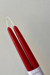 A pair of berry red beeswax taper candles against a white wall.