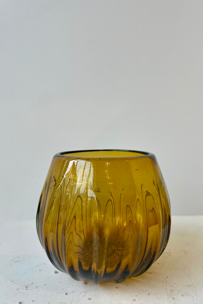 Stemless amber colored wine glass on a white surface in a white room