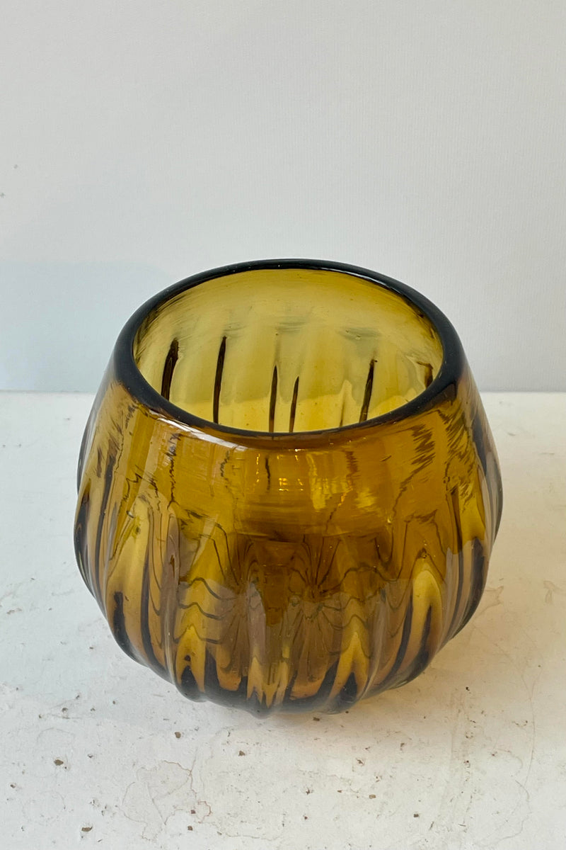 Stemless amber colored wine glass on a white surface in a white room