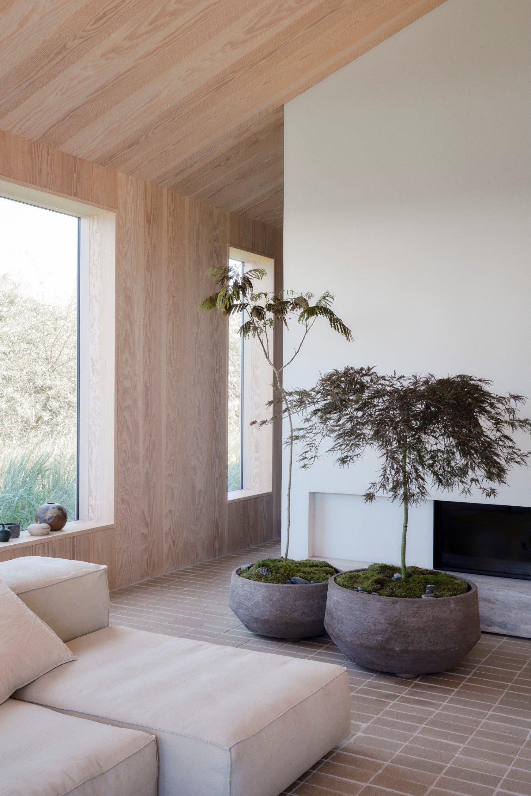 Modern living room with neutral decor, large windows, trees planted in Doma Grey pots and a fireplace. ©Bergs Potter