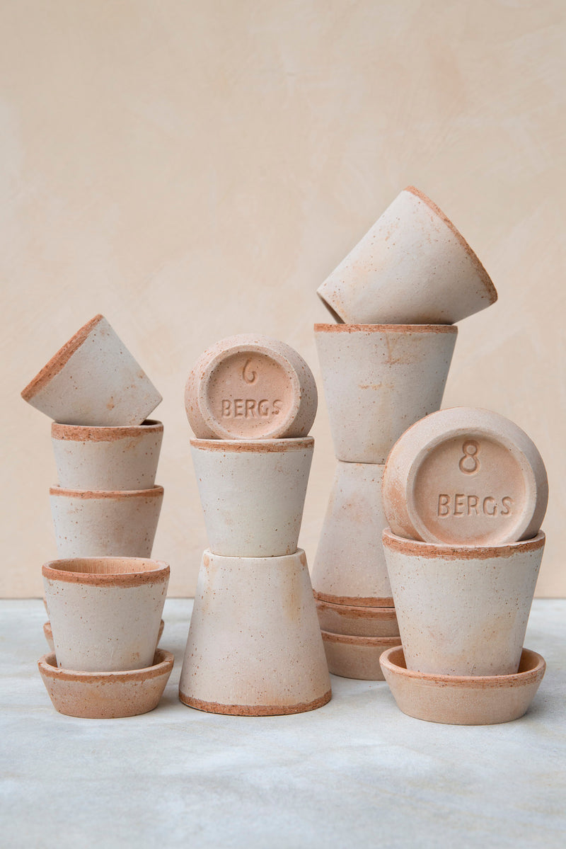 Various sized Rosa Julie pots and saucers by Bergs Potter against a peach backdrop.