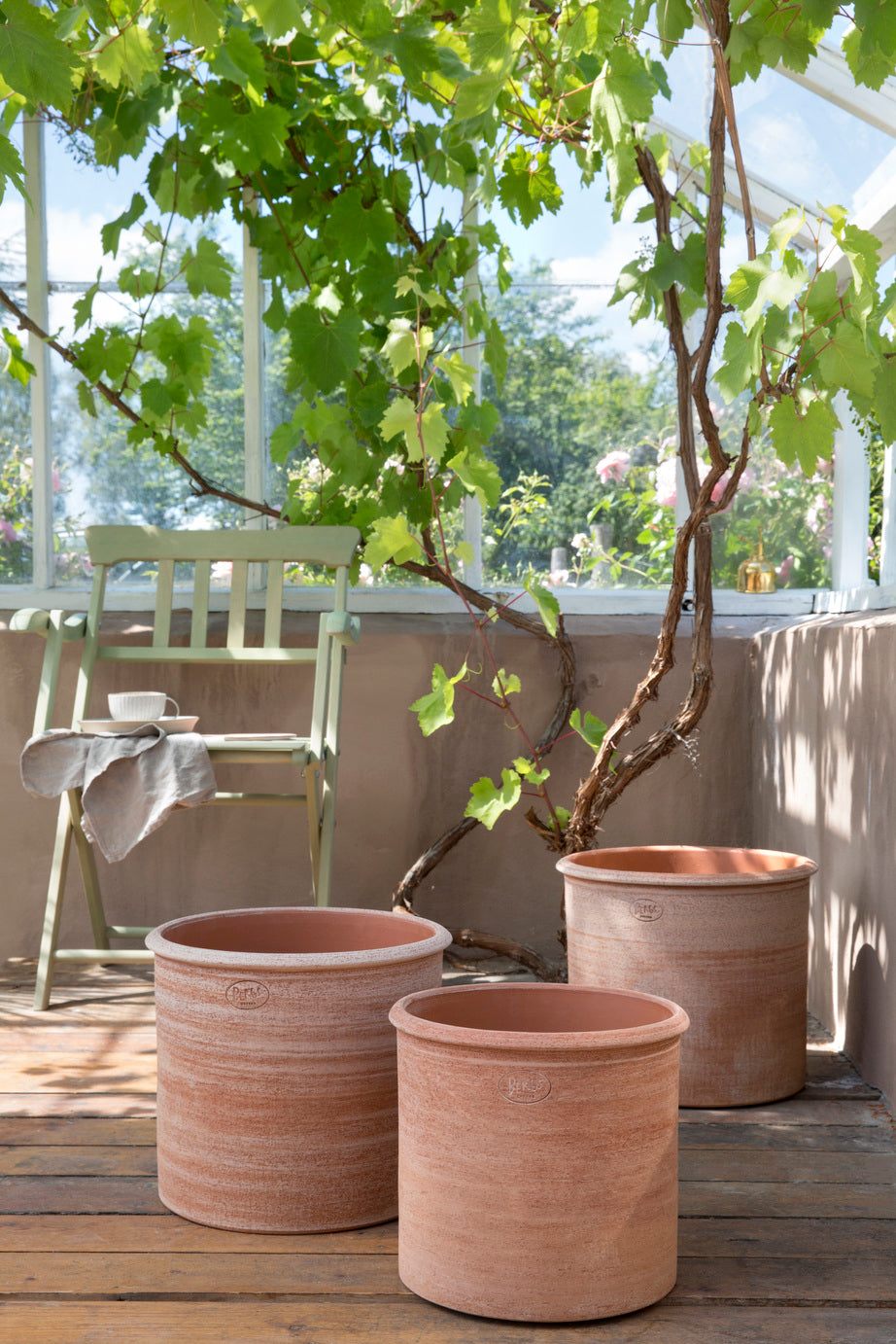 Three terracotta Rosa Modena pots with a plant on a wooden deck ©Bergs Potter