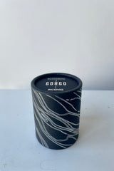 A black cylinder of Blackbird incense sits on a white surface in a white room. The package features undulating silver parallel lines. The incense is labelled Gorgo.