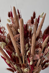 Photo of the Blind Date preserved floral arrangement with pink, mauve and berry colors preserved flowers against a white wall.