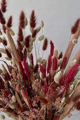 Photo of the Blind Date preserved floral arrangement with pink, mauve and berry colors preserved flowers against a white wall.