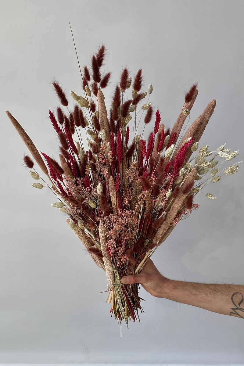 Photo of the Blind Date preserved floral arrangement with pink, mauve and berry colors preserved flowers against a white wall.