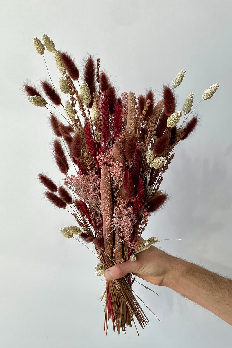 Photo of the Blind Date preserved floral arrangement with pink, mauve and berry colors preserved flowers against a white wall.